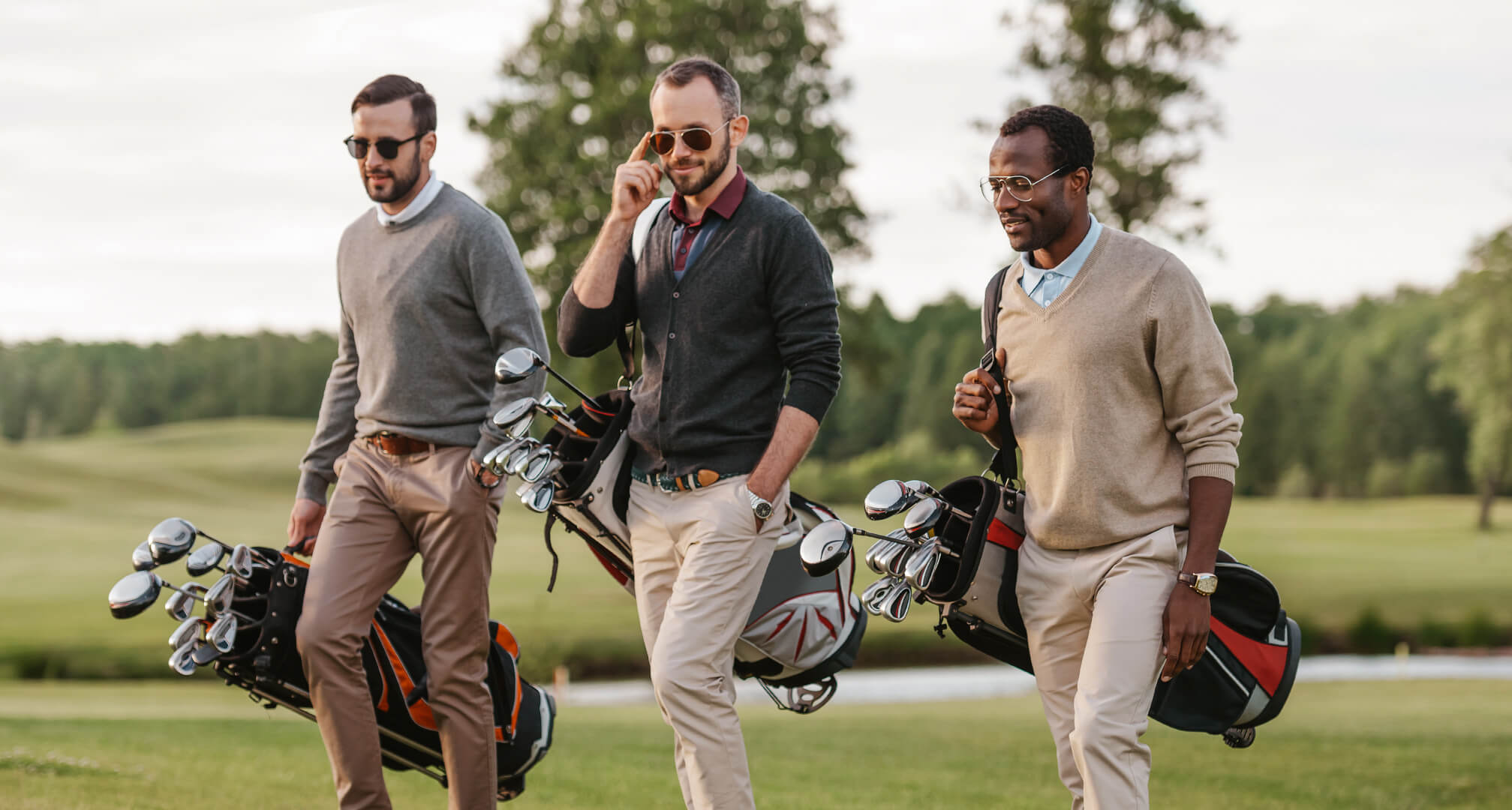 τρία άτομα παίζουν γκολφ φορώντας γυαλιά ηλίου και τσάντες του γκολφ